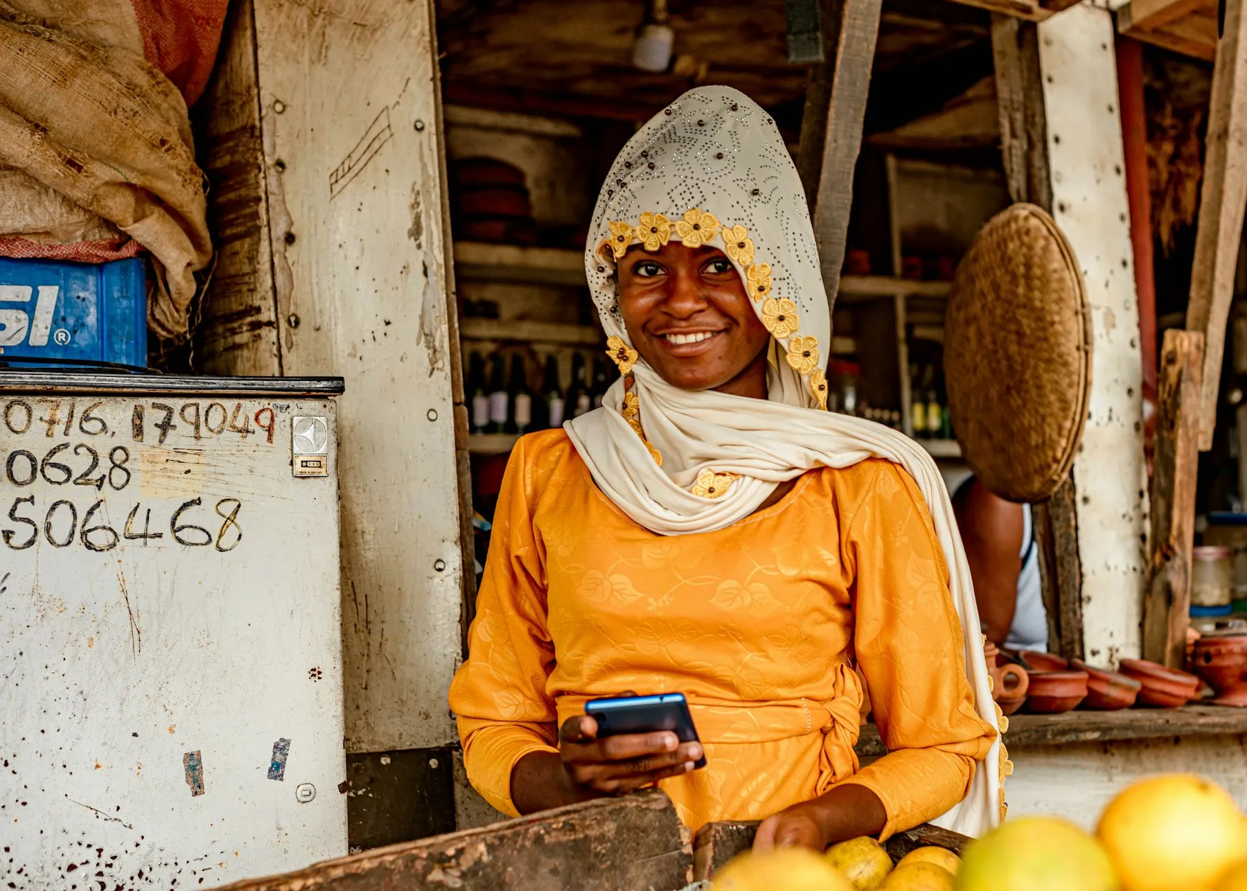 A smiling market vendor checking her phone at her fruit stall