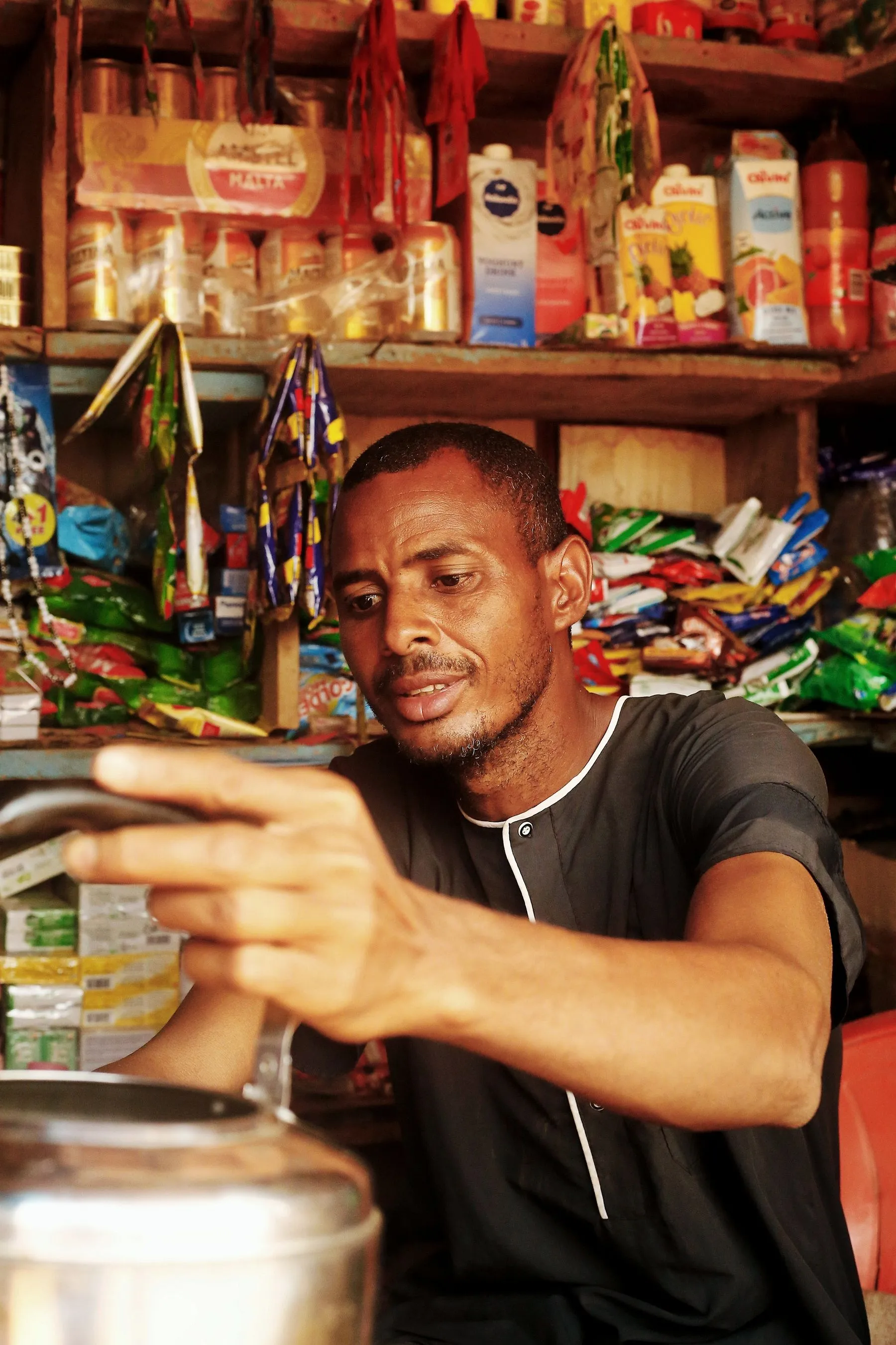 A shopkeeper reaching across the counter of his packed provisions shop