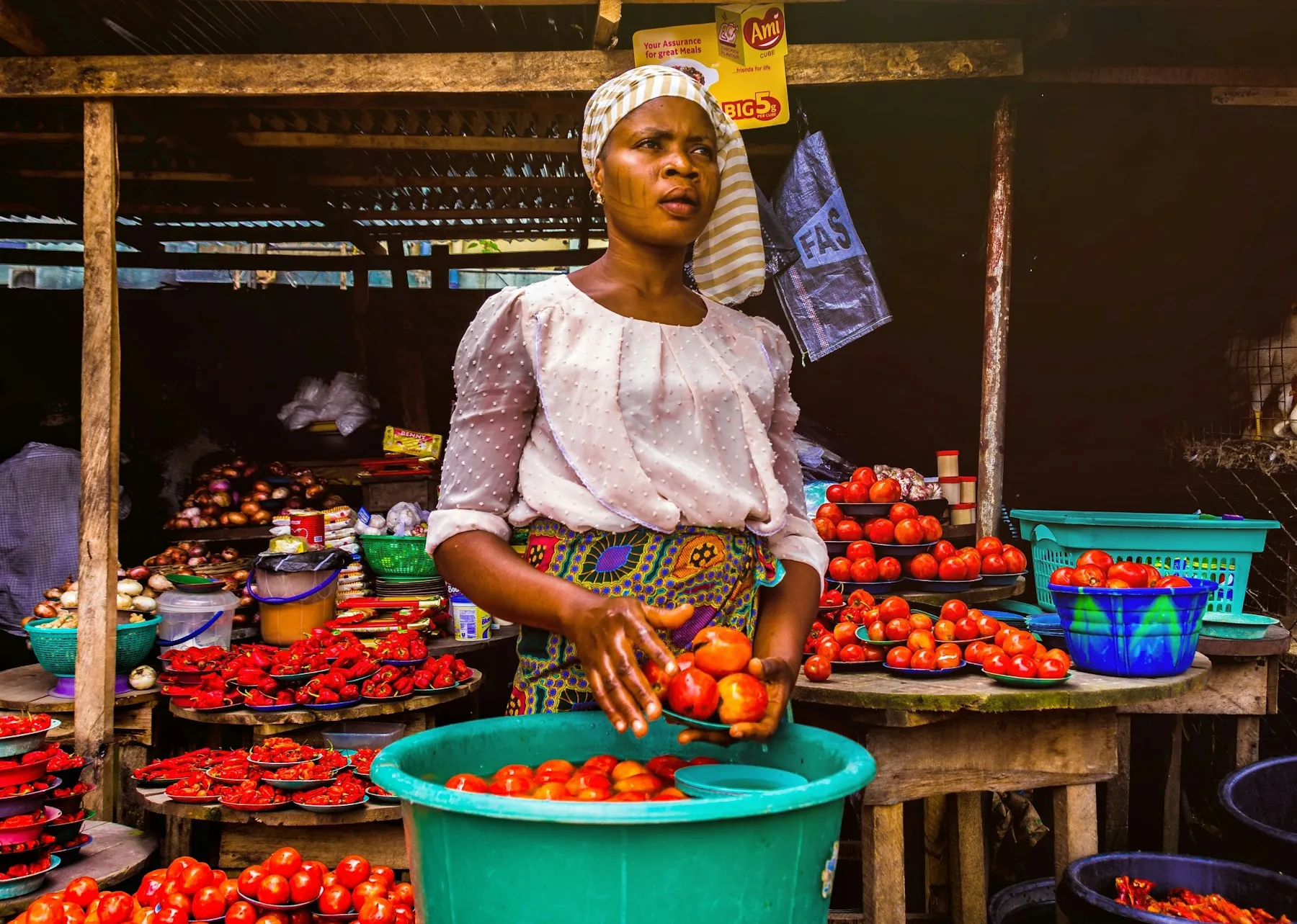 A market trader in a headscarf sorting tomatoes at her produce stall