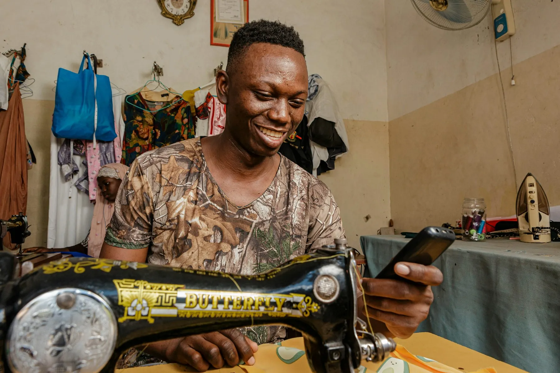 A tailor smiling at his phone while working at his sewing machine