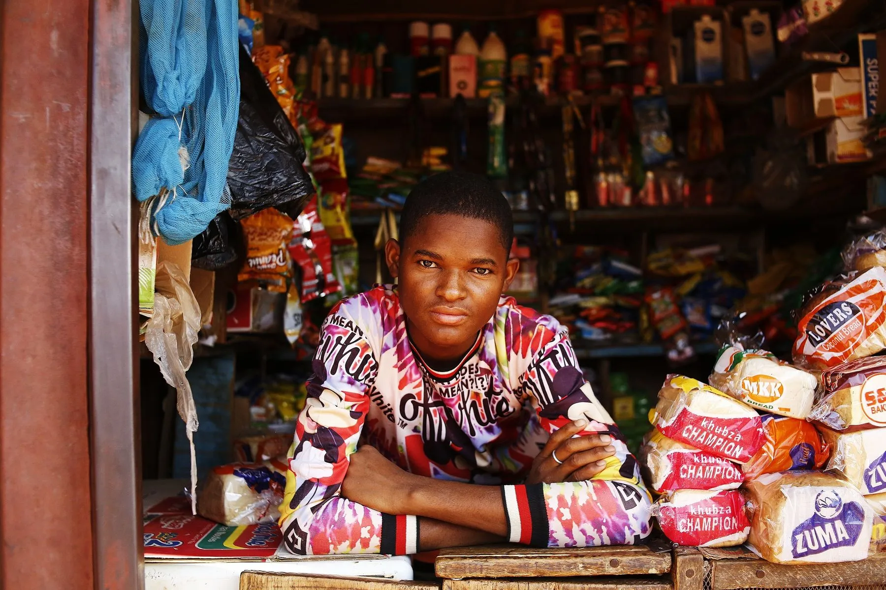 A young shopkeeper leaning on the counter of his grocery kiosk