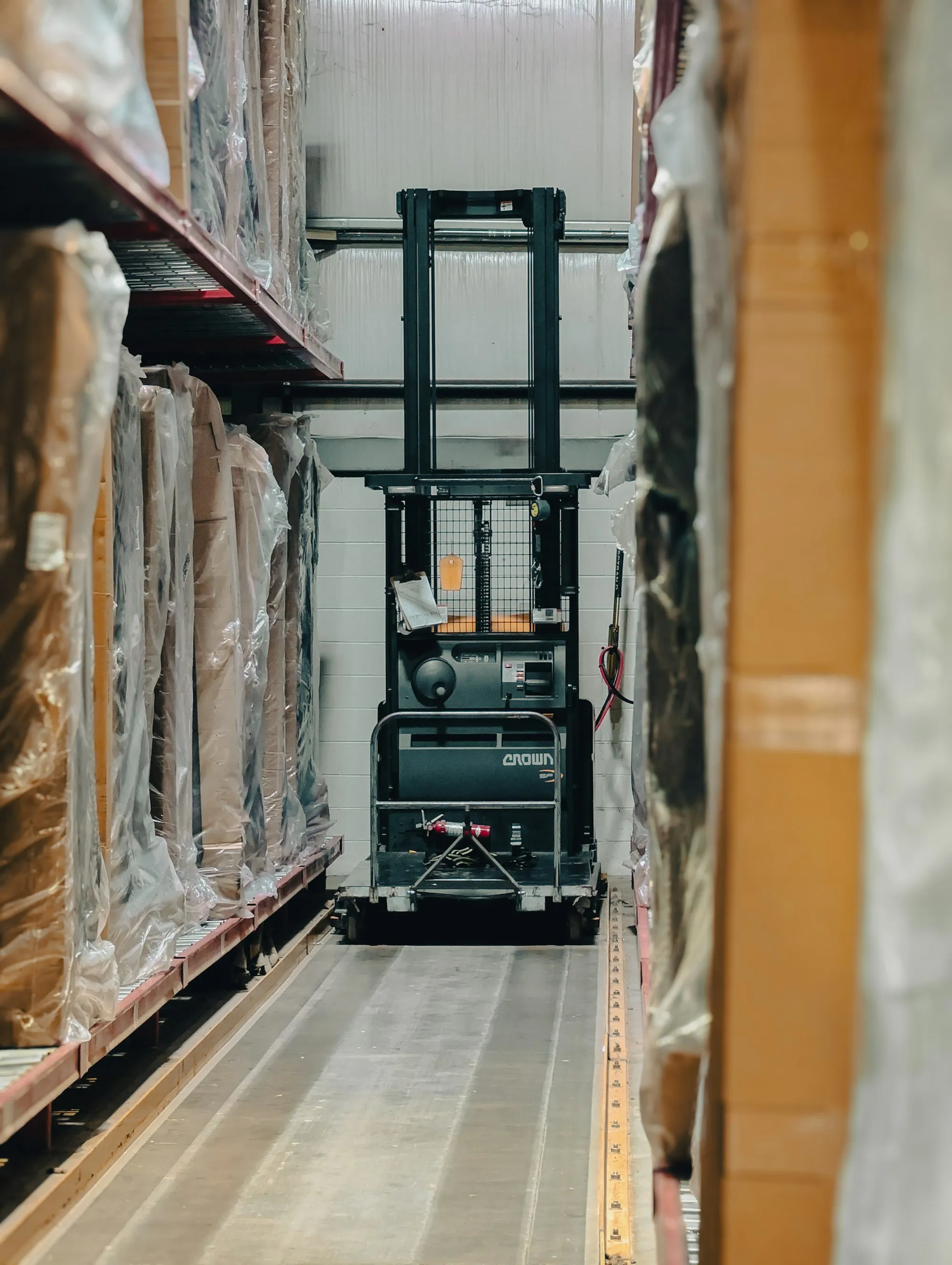A forklift in a warehouse aisle between racks of wrapped stock